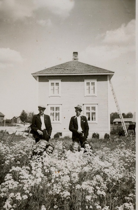 På bilden här ovan står Karl Lillkull t.v och Yngve Söderqvist och bland blommorna gömmer sig 4 unga damer, fr.v Elvi Långfors, Mildrid Forslin, Inga Klemets och Ewy Forslin. Bilden är tagen från väster, landsvägen syns till vänster på bild och i vänstra kanten syns lite av Dahlroos Arvids hus. I högra kanten syns uthusen hos Eskil Agnäs. 
