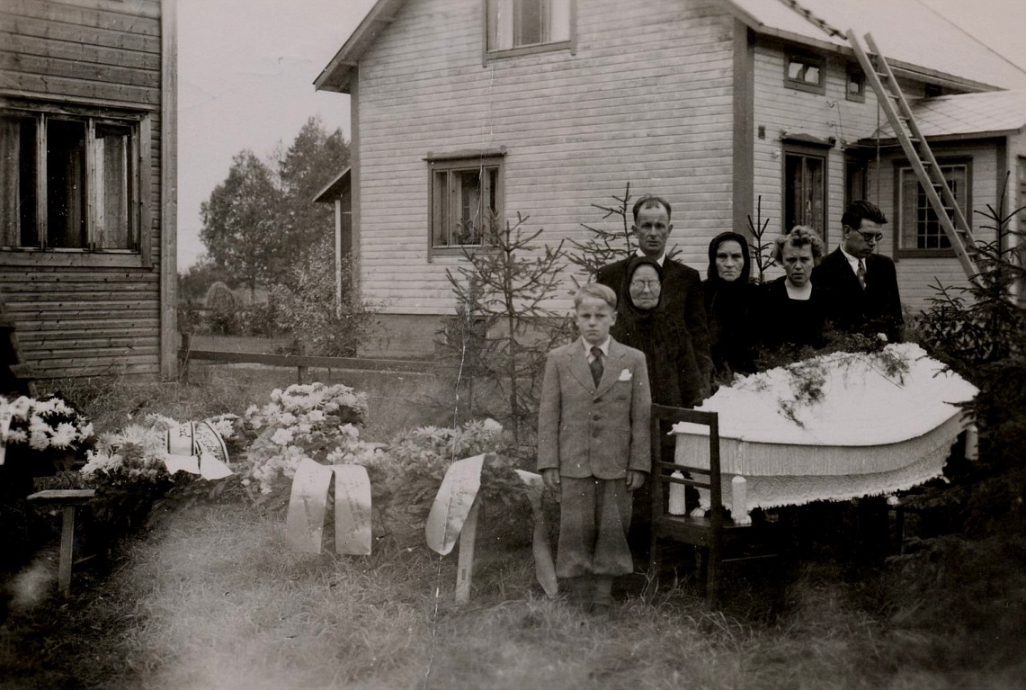 Vera Norén som var född år 1915 gifte sig år 1942 med Lennart Klockars (1912-1984) från Lappfjärd. År 1943 fick de sonen Max och de bodde i Dagsmark och sedan flyttade de till Kristinestad. År 1950 flyttade de till Lappfjärd då deras gård blev färdig i Idbäcken. År 1952 dog Vera plötsligt och här på fotot står sonen Max, som då var 9 år gammal. Bakom honom står hans farmor Maria ”Mina” Vilhelmina (1879-1959) och bakom henne står pappa Lennart. Bredvid Lennart står Fina Norén och till höger står Veras syskon Aina och Rurik. Huset i bakgrunden tillhörde Holger och Edith Hammarberg. Foto: Ilta-Lilja Klockars. 