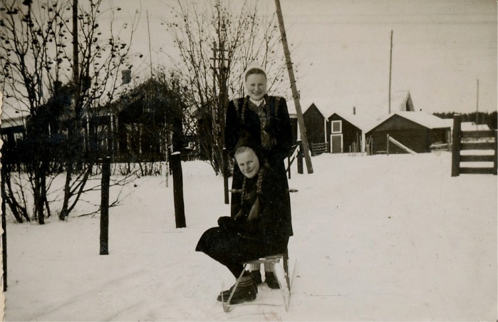 Bakom flickorna Verna Agnäs och Gerda Klåvus syns “Måg-Jåssas” eller Klåvus gård, fotograferad från öster. 