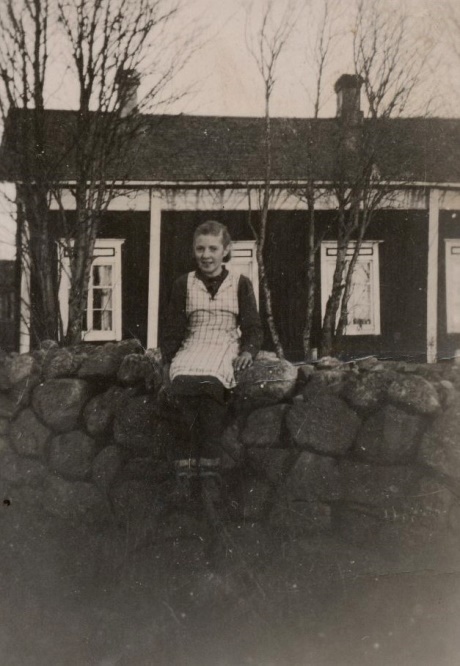 Agnäs-Henrik och Minas sytningsstuga stod med knuten mot landsvägen. Mellan stugan och landsvägen fanns en hög och vacker stenmur, som grannflickan Alice Björklund har klättrat upp på. Fotot från 30-talet är taget från väster.