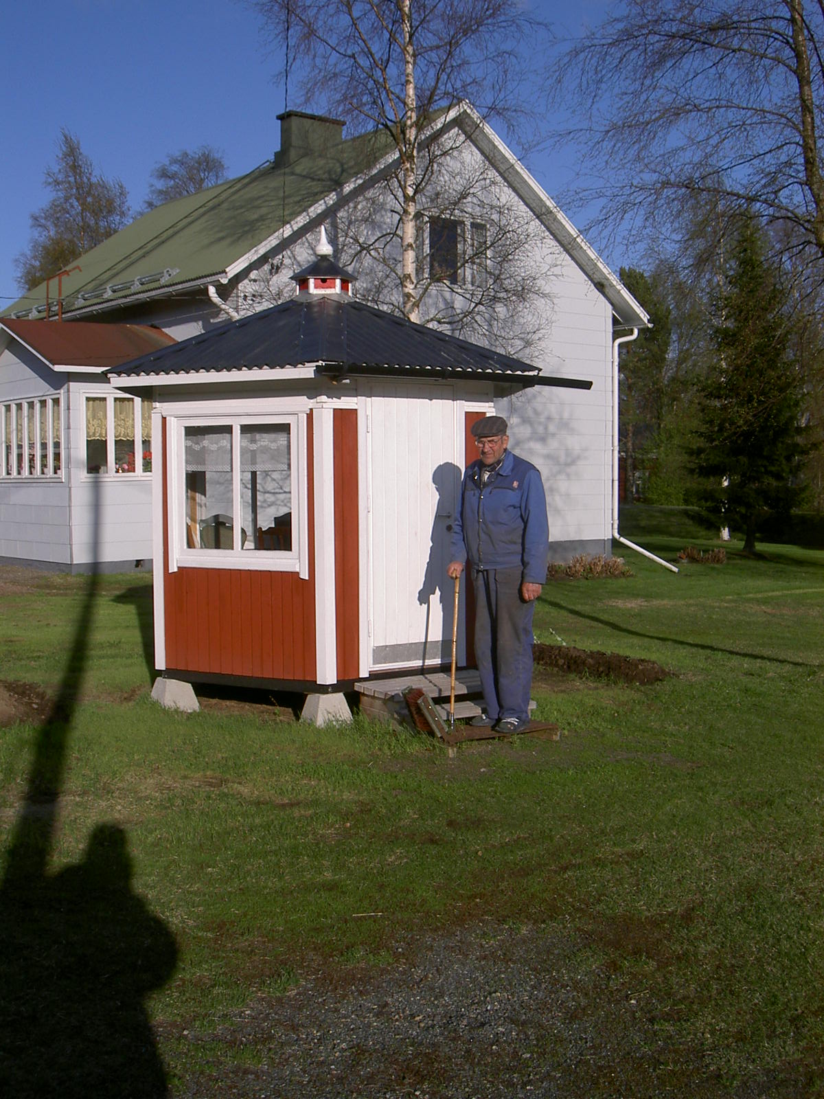 Här står Arvid Dahlroos framför det egenhändigt byggda lusthuset där hemma på gården, året är 2003. I bakgrunden Else Korsbäcks gård.