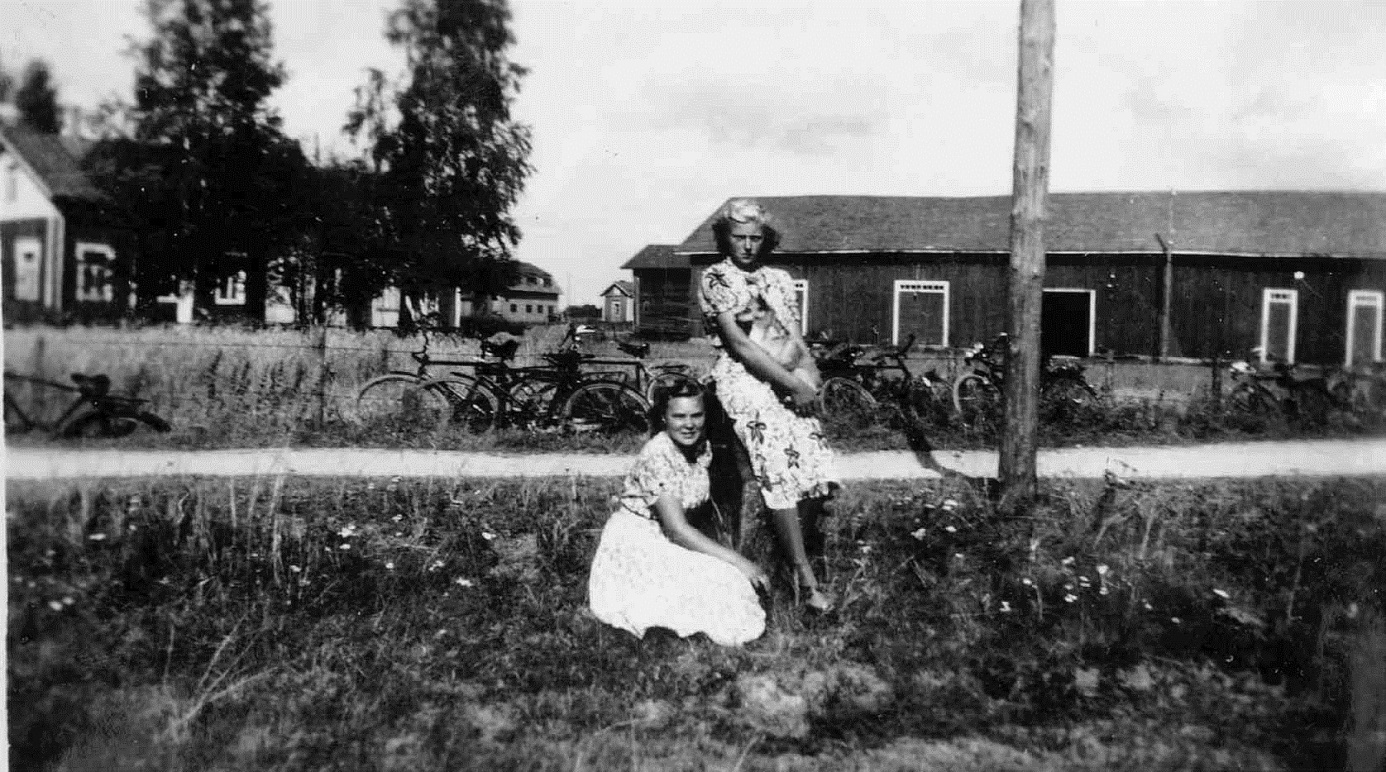 På bilden från 1950-talet ser vi Eklunds gamla gård i bakgrunden t.v. , mitt i bild skymtar Westaras smedjan och Koll-Minas gård. Det är Greta Gröndahl, gift Lindell som sitter och Ruth Mitts som står med hunden Nelly i famnen. Notera de många ”karavangnen” på andra sidan Lillsjövägen.