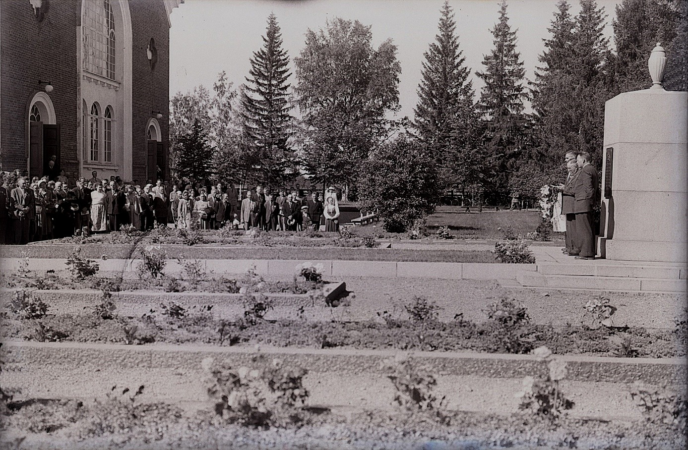 Här på Selim Björses foto är det en högtidlig uppvaktning vid krigargravarna framför kyrkan i Lappfjärd. Minnesmonumenten till höger i bild restes efter inbördeskriget, ungefär 1920. Det är tillverkat i Hangö och transporterades därifrån med tåg till Kristinestad och sedan med häst till Lappfjärd. Traditionsarkivet i Vasa.