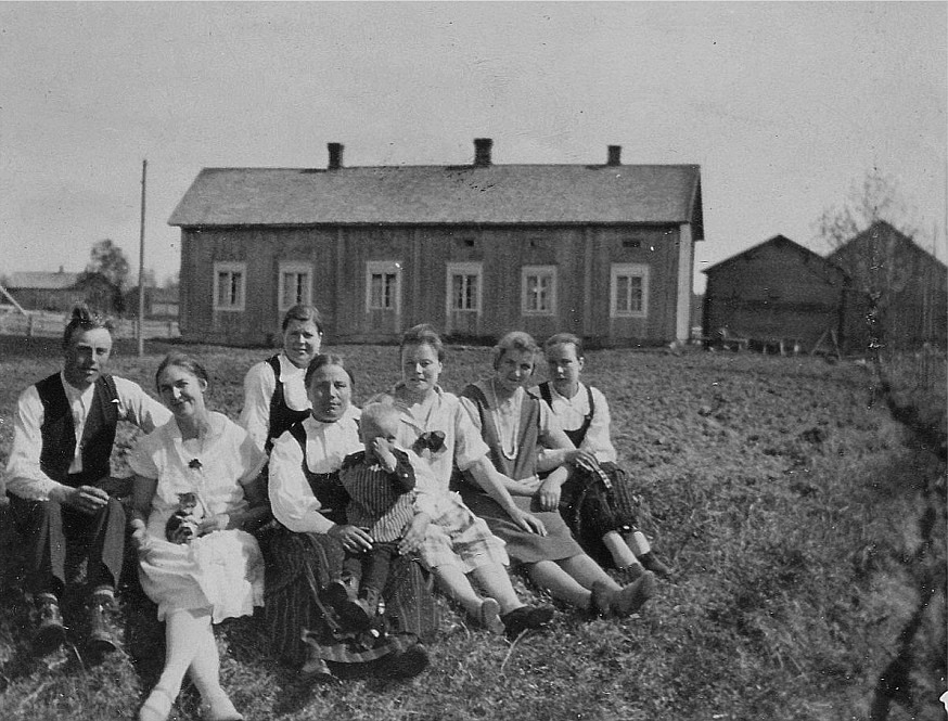 Fr.v. Anselm Lillkull (1902-1962) och hans dåtida fästmö Daga Kjellberg, hemma från Nykarleby som var lärare i Dagsmark åren 1925-1929. Den äldre damen mitt i bild är Adelina Lillkull (1876-1947) och snett bakom henne sitter sonhustrun Amanda (1904-1989) som var gift med Adelinas son Selim. I Adelinas famn sitter Nils Lillkull (1925-2002). Till höger om Nils sitter Aina (1904-1989) som gifte sig med Sigurd Löfgren. Längst till höger sitter Signe Ekberg (1909-1990) som gifte sig med Leander Nyholm. Men vem sitter bredvid Signe, andra från höger? Huset fotograferat från nordost år 1928. 