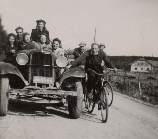 Åke Jossandts biltraktor var speciell och många ville vara med och provköra men alla rymdes inte med. Från vänster Birgit Englund, okänd man, Dagny Lillkull, stående Gunvor Hemberg och framför henne sitter systern Else-Maj och till höger sitter Greta Gröndahl. Cyklisterna från vänster är läraren Einar Lind, Bengt Gröndahl och lite skymd Åke Löfgren. I bakgrunden syns uthusen hos Hembergs.