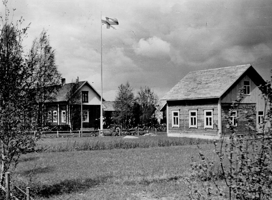 Där ”Jöranas” eller hos Erland Norrgård flaggades det hösten 1941 då dottern Svea gifte sig med grannen Gunnar Guss. Till höger ser vi lillstugan, alltså den dit Heikki och Ulrika Henberg flyttade i november 1907. Troligen hade lillstugan tidigare stått på en annan plats på samma tomt. Här ser vi att lillstugan som bäst skarvas i både på gårdssidan och med större vindsutrymmen, då Erland och Ida Norrgård flyttade in.