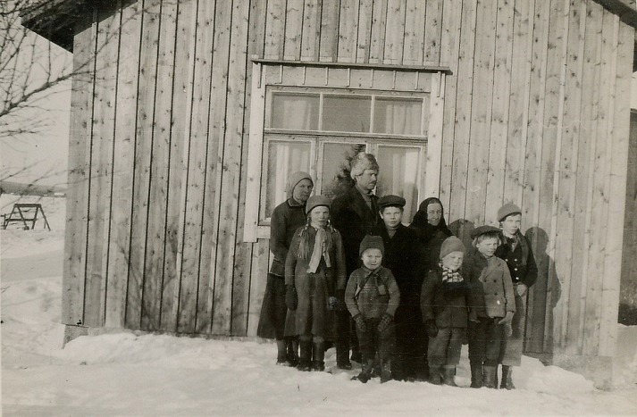 På detta foto från år 1935 ser vi nästan hela Hällbacks familj, där de står utanför lillstugan som byggdes ungefär 1932 och som sedan på 1940-talet byggdes i med en port, ett kärrlider och ett vedlider. Längst bak fr.v. Hilma och Johannes Hällback, Hilmas mor Amanda Uusitalo och längst till höger Sylvi Hällback. Flickan och pojken i mittersta raden är Elvi och Alvar Hällback. I främre raden Aarre, Pauli och Jarl. Minstingen Pentti var inte född ännu när detta foto togs. 