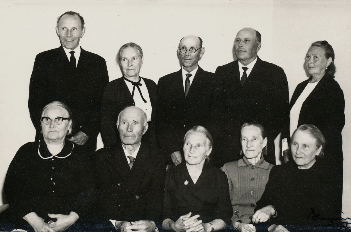 Nere t.v. Alvina (1889-1982) som gifte sig med Erland Rosenback , följande Johannes (1891-1970) som gifte sig med Hilma Elvira Ojanperä från Storå och som tog namnet Hällback, Maria Vilhelmina (1893-1989) som gifte sig med Sigfrid Storlåhls från Måston eller Lillsund, följande Alma (1895-1984) som gifte sig med Emil Nyberg och längst ut Amanda (1897-1985) som gifte sig med Evert Gröndahl. Stående fr.v. Viktor (1899-1981) som först varit gift med Helmi Tuominiemi men som sedan gifte sig med Selma Nyberg och som tog namnet Berglind, följande är Jenny (1901-1976) som var ogift, följande Leander (1904-1972) som gifte sig med Selma Hammarberg, sedan Arthur (1905-1985) som gifte sig med Helmi Lydia Jansson från Storå och längst t.h. Mathilda (1908-1984) som gifte sig med Emil Lillsjö. 