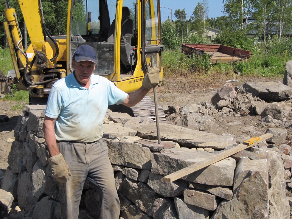 Stora stenar skall flyttas och lyftas med grävmaskin men här visar Jukka upp järnspettet som alltid skall användas för att få stenarna att ligga rätt.