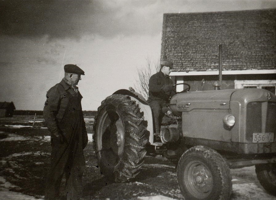 Emil Nyholm står och ser på, då mågen Lars Ålgars kör traktorn.