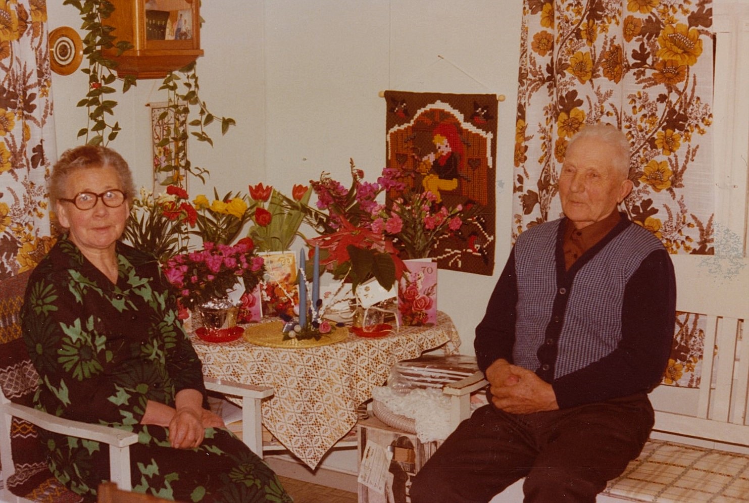 Här sitter Hulda och Emil Nyholm och av korten bland blommorna att döma är det någon av dom som fyller 70.