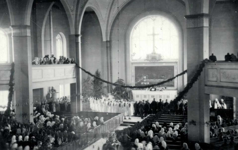 Konfirmanderna står i dubbla rader framför altaret i Lappfjärds kyrka. Ett par dagar på förhand hämtade konfirmanderna enris i skogen, som de dekorerade kyrkan med. Altaret dekorerades med björkar, som man gjorde förr i midsommartid.