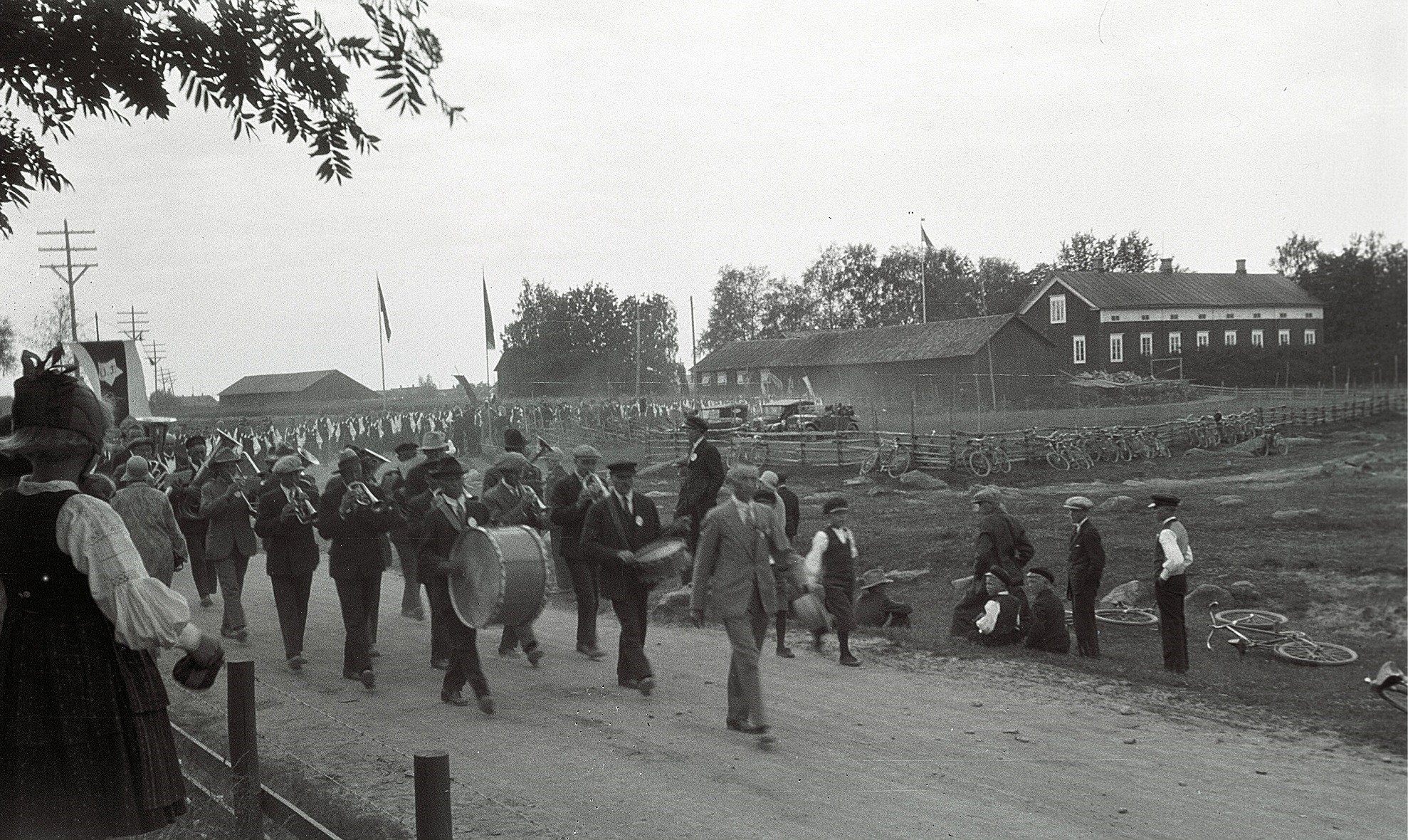 En lång rad med sångare och musikanter på väg från kyrkan till ungdomslokalen under sångarfesten i Lappfjärd 1930. Till höger syns Starkes eller nuvarande af Hällströms gård.