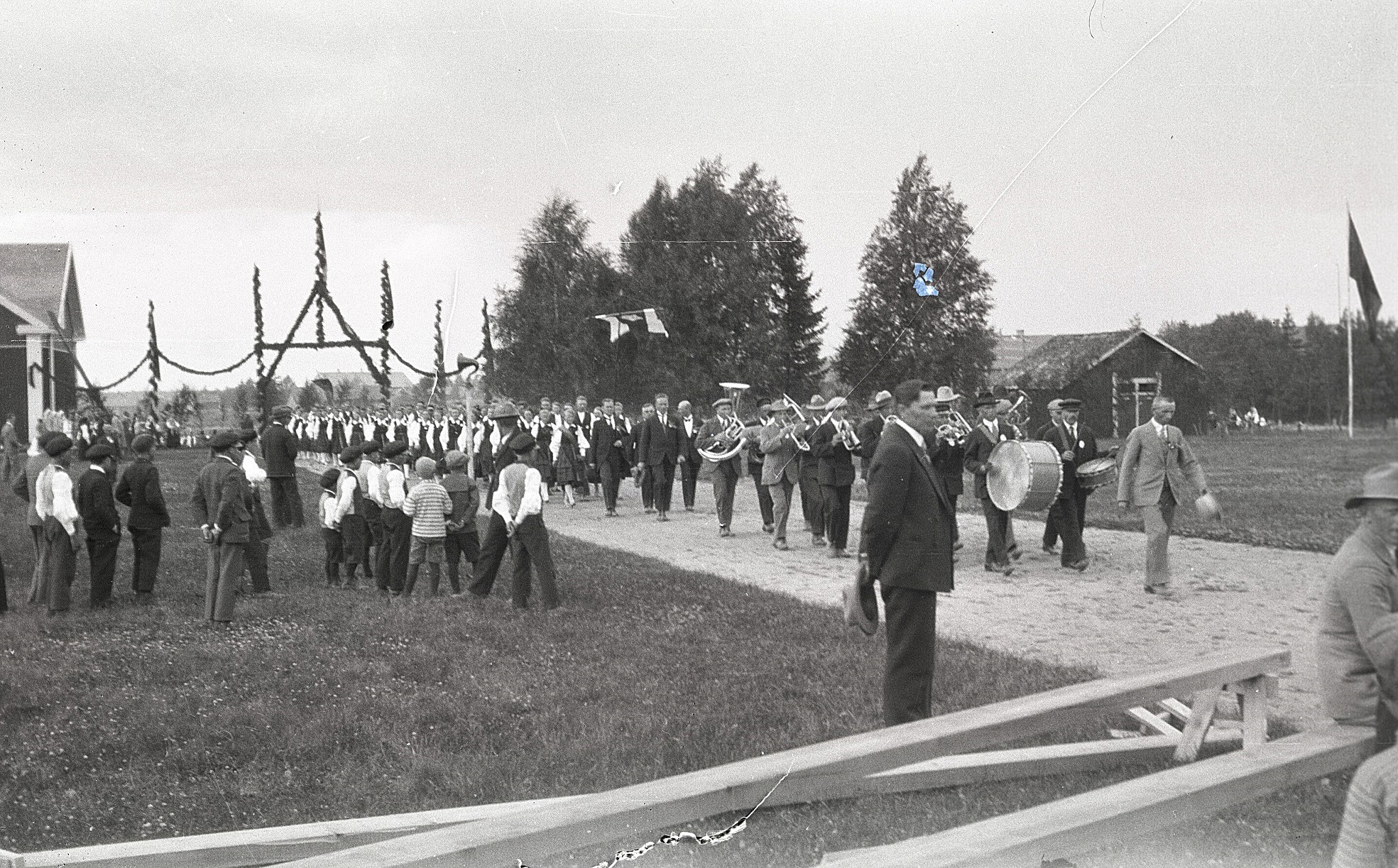 En lång rad med körsångare ledda av musikanter har just tågat in på festplatsen bakom ungdomslokalen som skymtar till vänster.