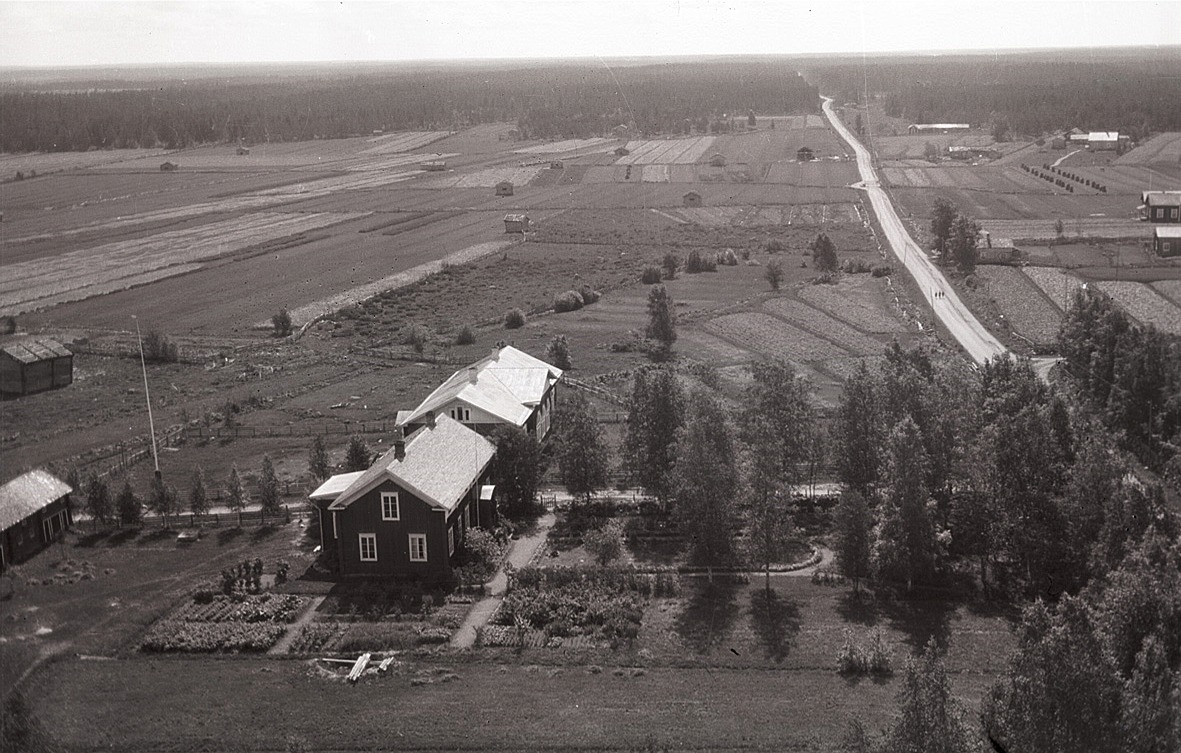 Foto taget från kyrkstapeln eller kyrktaket söderut med lärarbostaden och södra folkskolan. Folkskolan fortfarande utan vinkeltillbyggnad, notera speciellt den fina trädgården runt lärarbostaden.