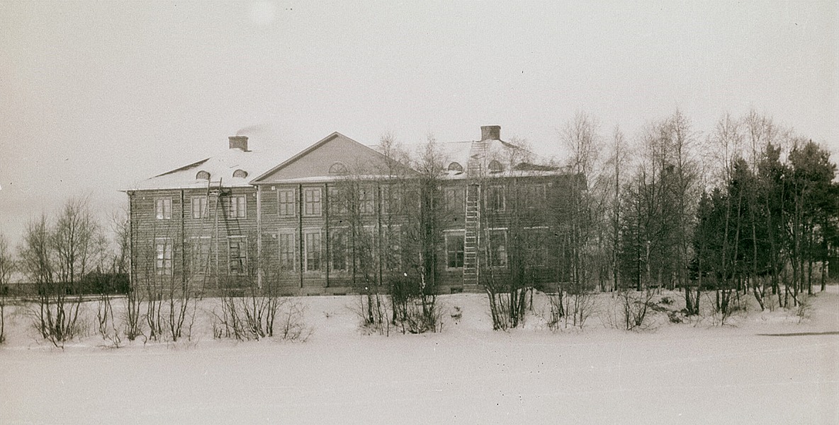 Röken stiger ur skorstenen på den nya folkskolbyggnaden, här fotograferad från andra sidan ån.