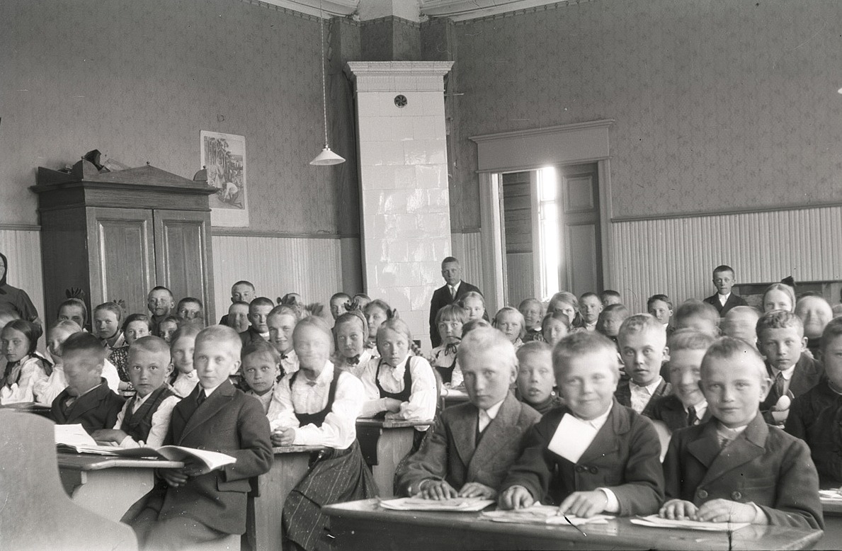 Eleverna på södra folkskolan ser alla glada ut och undra på det, då skolan är slut och sommarlovet på kommande. Läraren Selim Björses står bak i klassen.