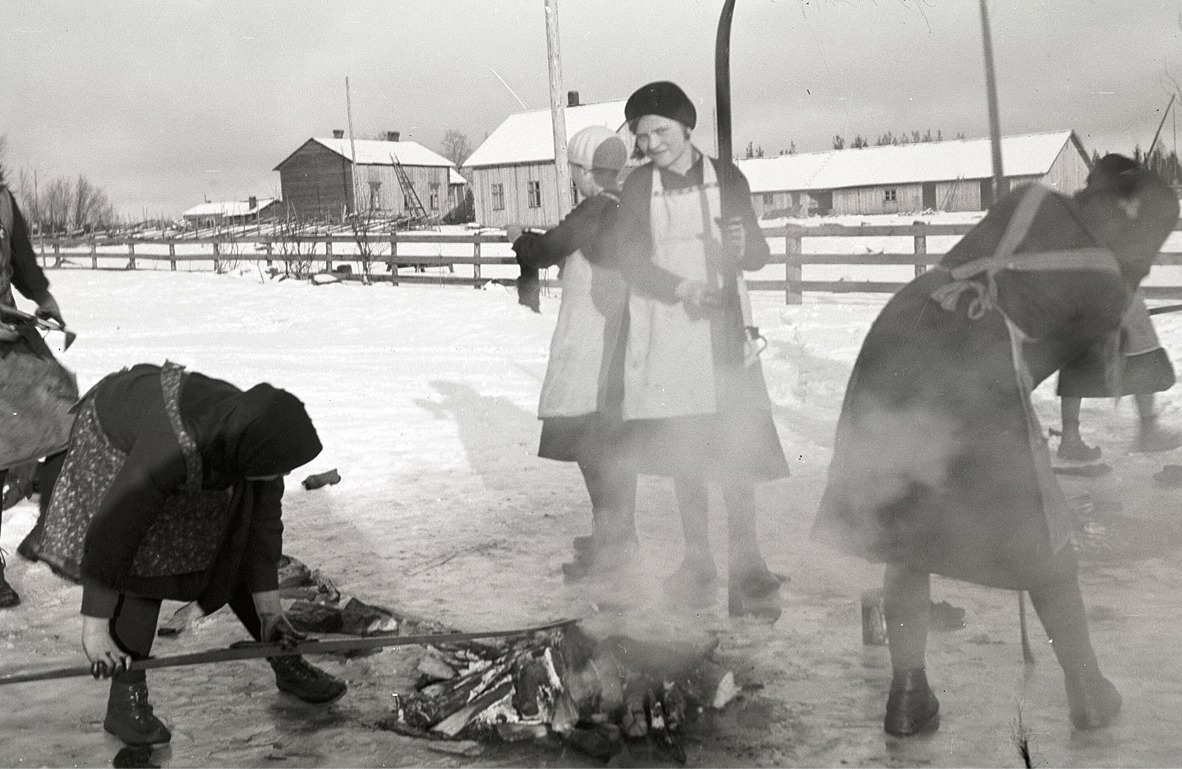 Här håller flickorna på och tjärar skidorna på vårvintern 1934, i bakgrunden "Gustas Kalas" gårdar. Flickan mitt i bild är Anni Norrholm men notera speciellt hur flickan till vänster har tjära på händerna!