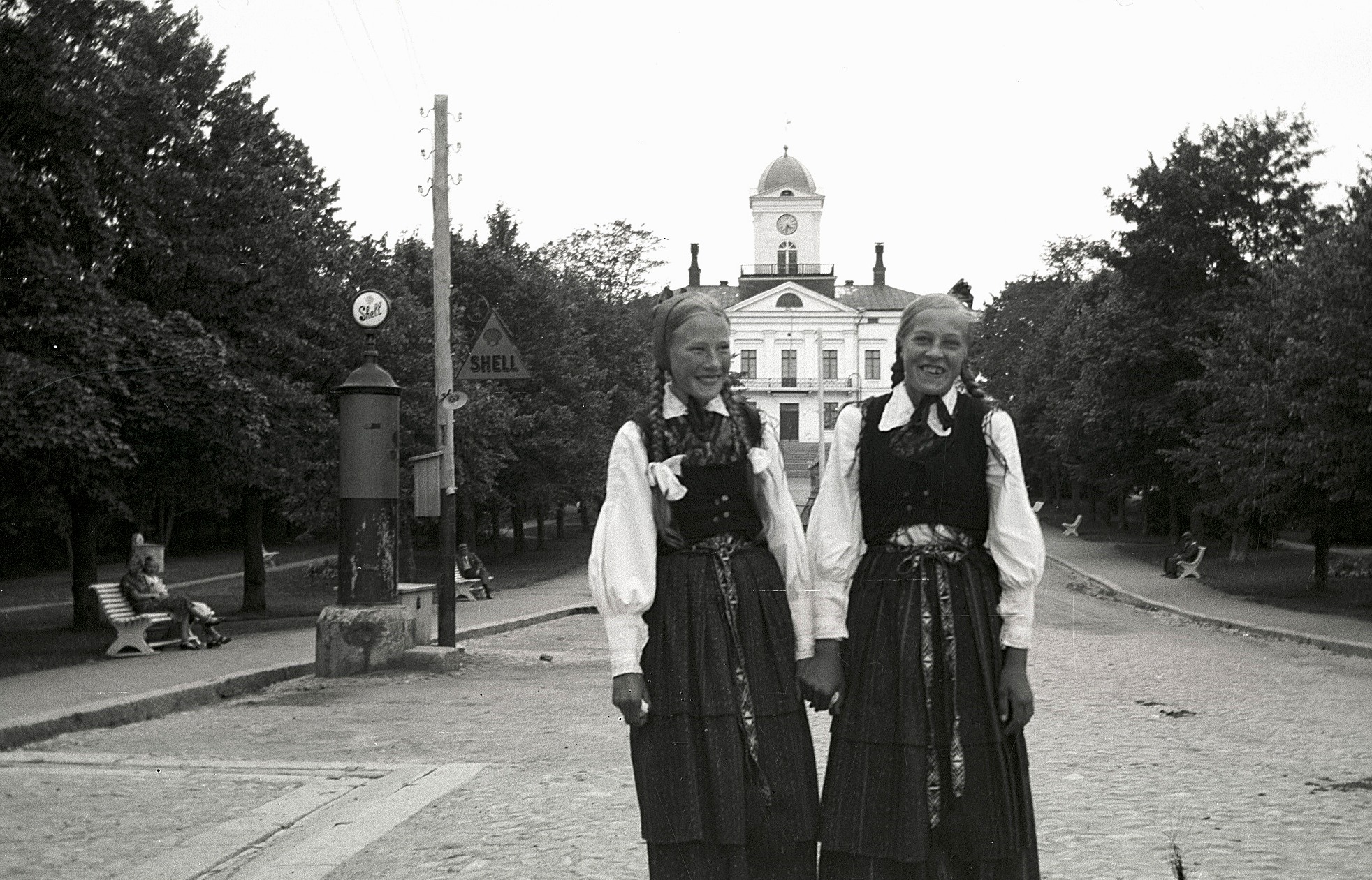 Ines Klockars och Alice Klockars i Rådhusparken i Kristinestad iförd vackra lappfjärdsdräkter. Notera den speciella bensinpumpen till vänster.