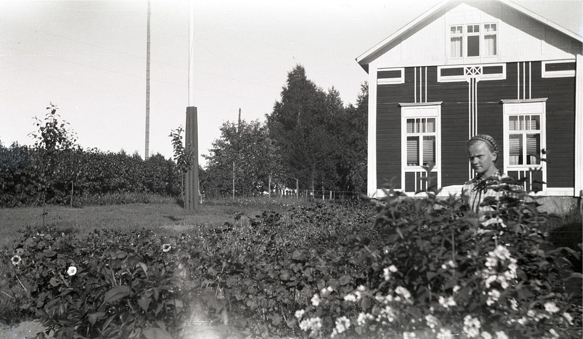 Verna Agnäs (f. 1925 senare gift med Arne Björkskog) visar upp sin fina trädgård, framför en minst lika fin bondgård på Sebbasbackan bredvid folkskolan i Dagsmark.