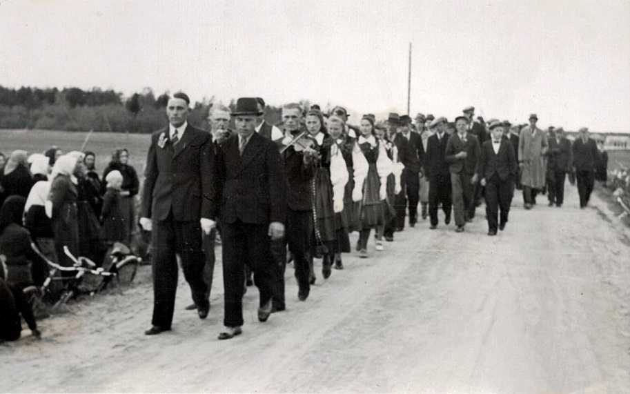 Här är Gunnar Guss på väg för att hämta bruden tillsammans med spelmän och bröllopsgäster. Mannen med hatten bredvid Gunnar är Bertel Långfors.