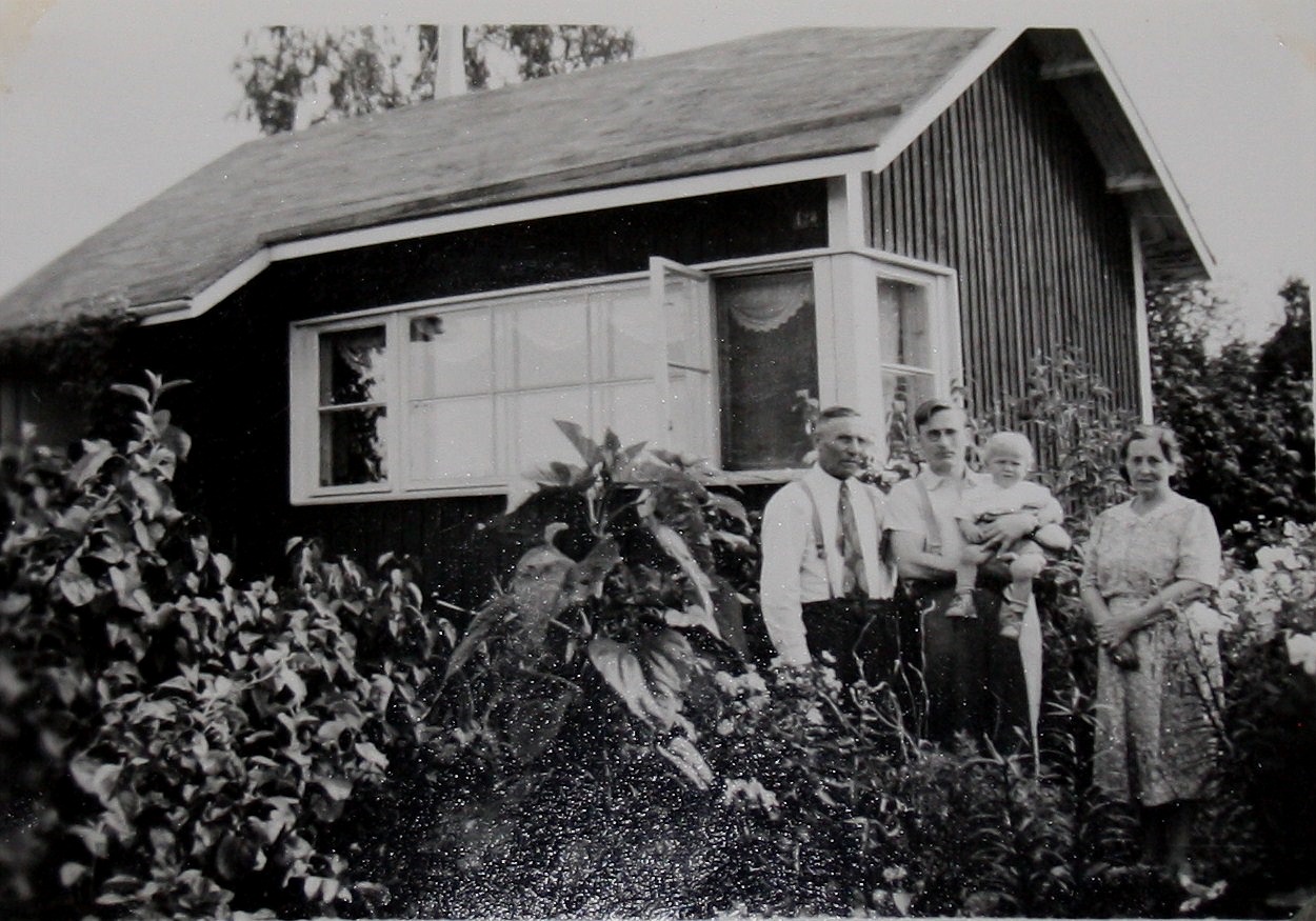 Här står Emil Båsk utanför kolonistugan tillsammans med Wilhelm med sonen Gustav i famnen, till höger står Ida Båsk. 