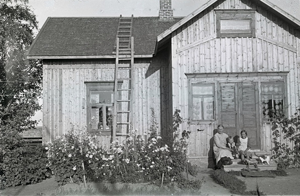 Alvina Björses sitter på brotrappan där hemma tillsammans med 2 barnbarn, en katt och en trähäst som går på hjul.