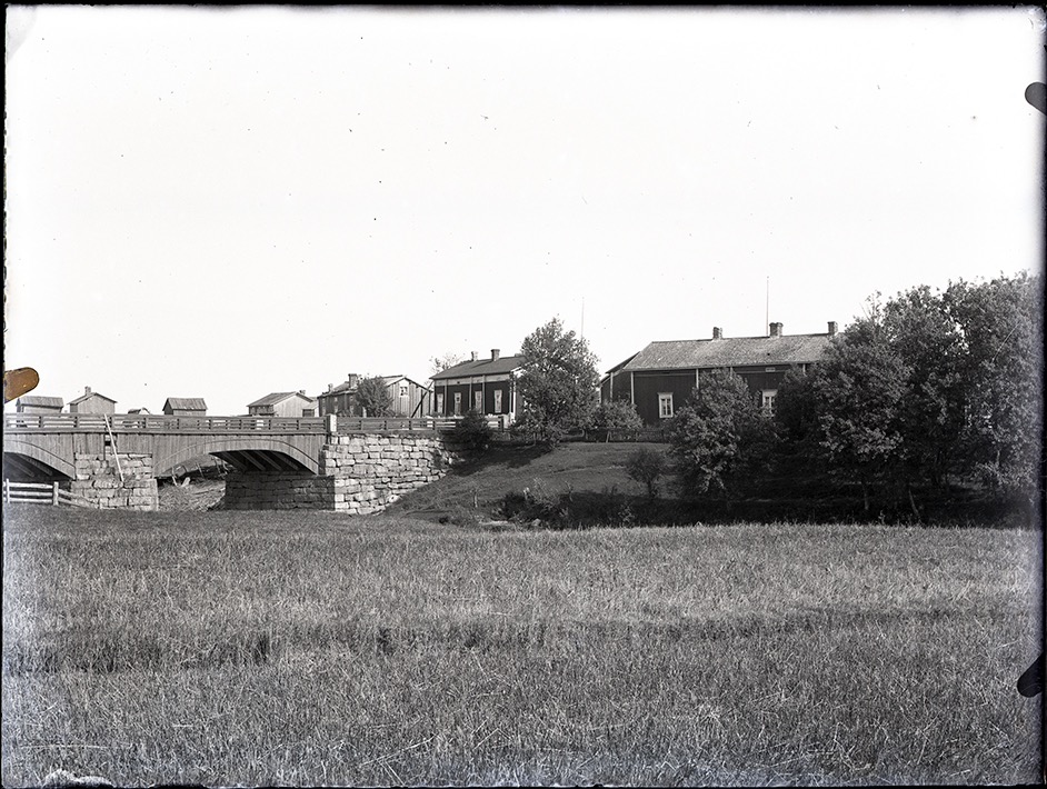 På det här fotot från ca 1915 ser vi hur den gamla gården på Åddin såg ut. Huset mitt i bild är ”Kork”-Frans Eklund gård som den såg ut före den byggdes på med en våning till. Följande gård är högst troligt den första gården som Långarna byggde på Brobackan i början på 1800-talet. Storbron till vänster byggdes 1855 och här ser vi hur brolocket i trä såg ut.