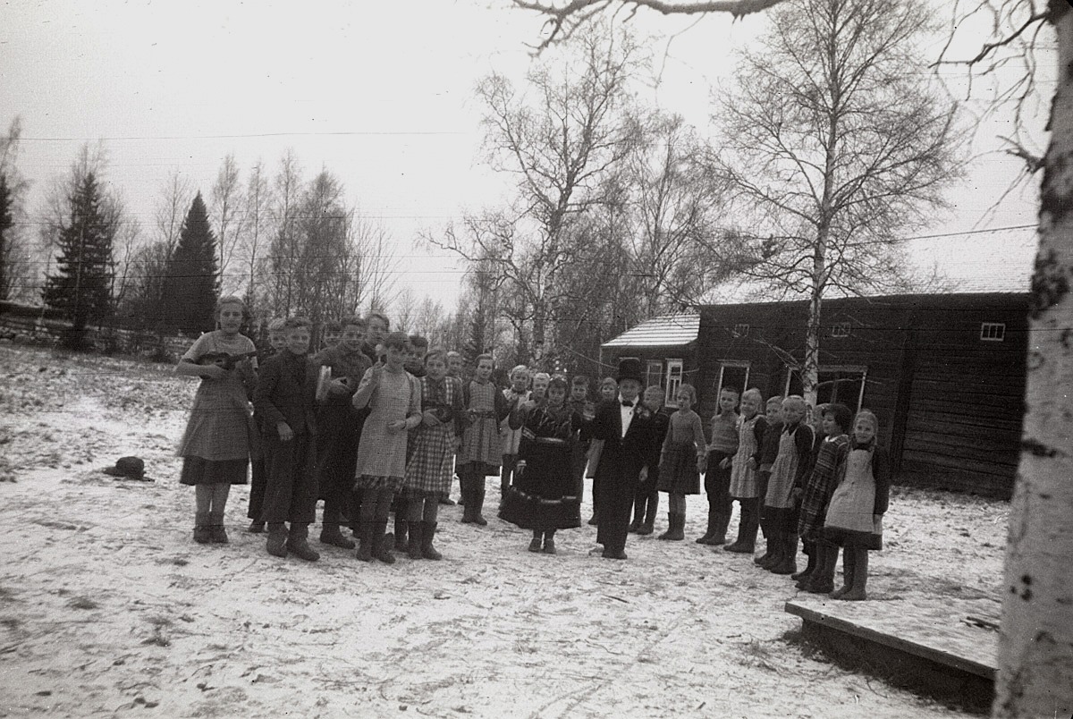 Här på skolgården övas det inför julfesten 1953, då brudparet Solveig Lärka och Torolf Söderlund skall framföra ett riktigt lappfjärdsbröllop. Orkestern är med, liksom "pellhaldaren" och gästerna. I bakgrunden skolans bastu och lider.