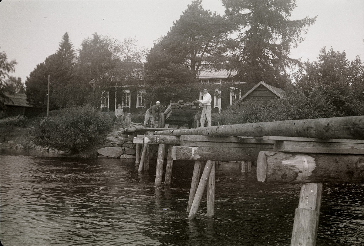 Ett säkert vårtecken var det då "Gamälbroen" skulle läggas ut. Här är det K. A. och Nils Björklund som visar åt barnen på stranden hur arbetet går till. I bakgrunden lantmätare Nils Molanders gård.