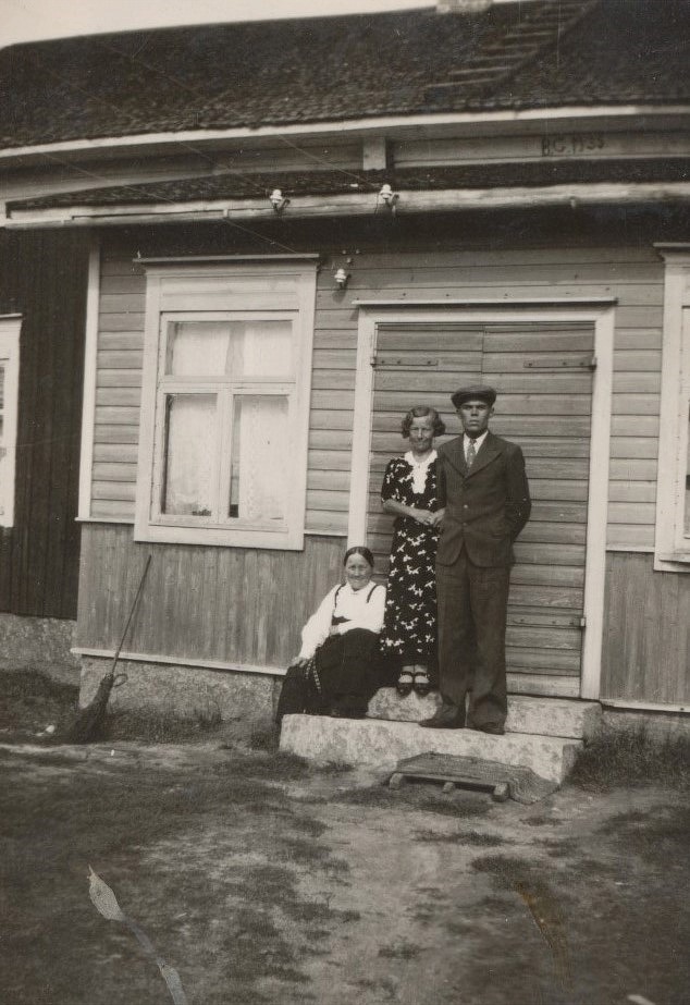 Signe och Lennart Grans står finklädda på trappan medan Signes mor Selma är klädd i folkdräkten. Under utskeftet står årtalet 1935 och det kan betyda det år då gården byggdes om och fick en ny stenfot.