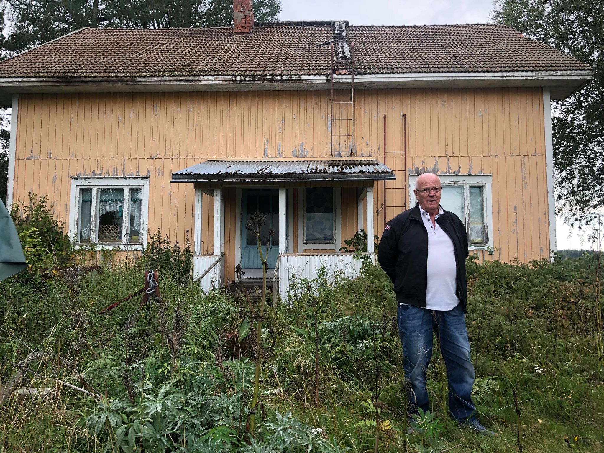 Roy Rosenback utanför den förefallna hemgården dit han flyttade som 6-åring och där han bodde i 10 år före han flyttade till Sverige.